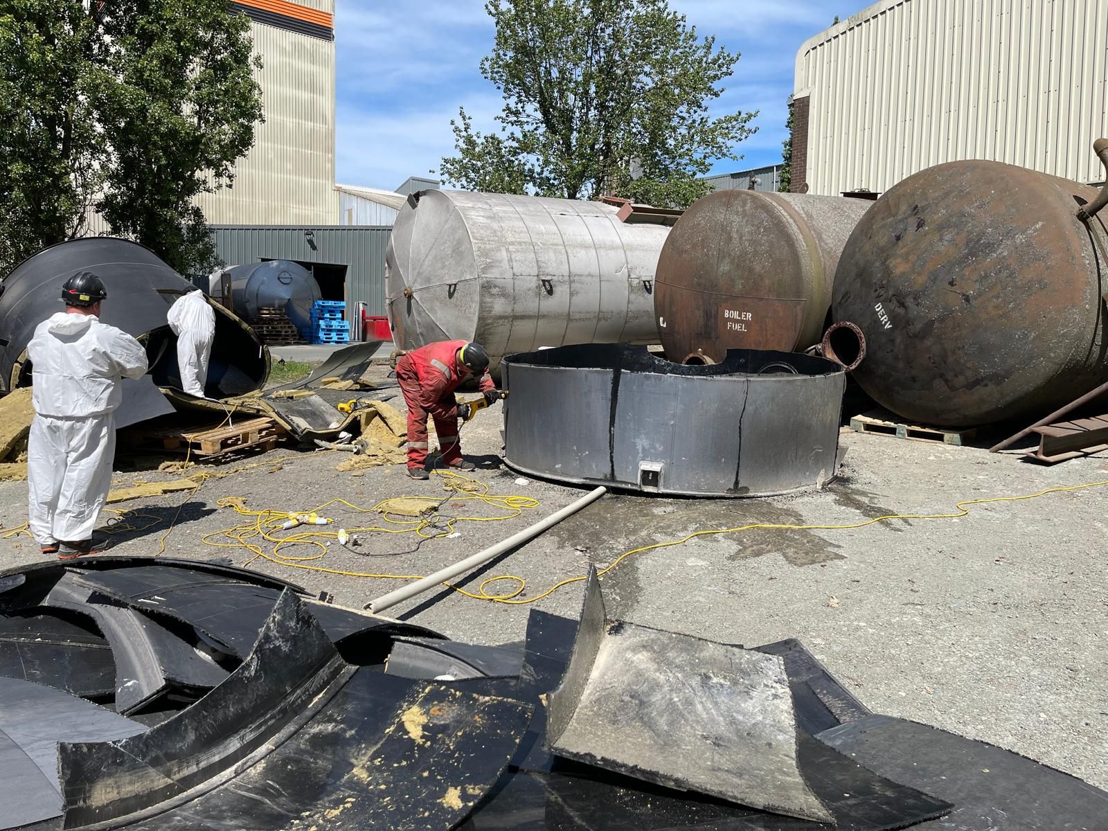Operatives in protective coveralls cutting down redundant storage tanks in a yard during a decommissioning project.