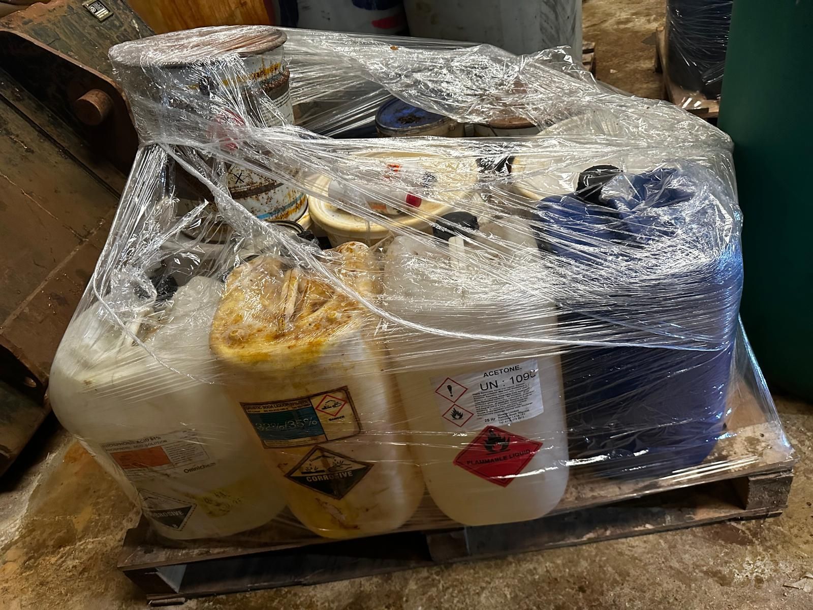 A wrapped pallet of chemical containers prepared for collection during a site clearance.