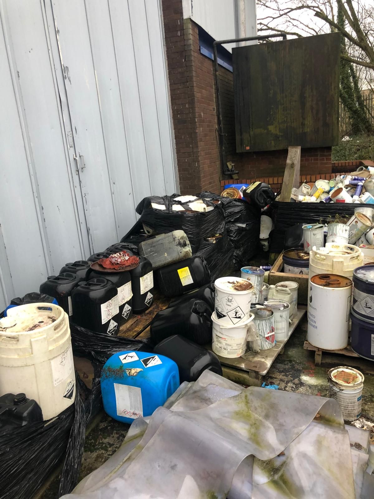 Labelled waste containers standing ready for collection outside an industrial unit.