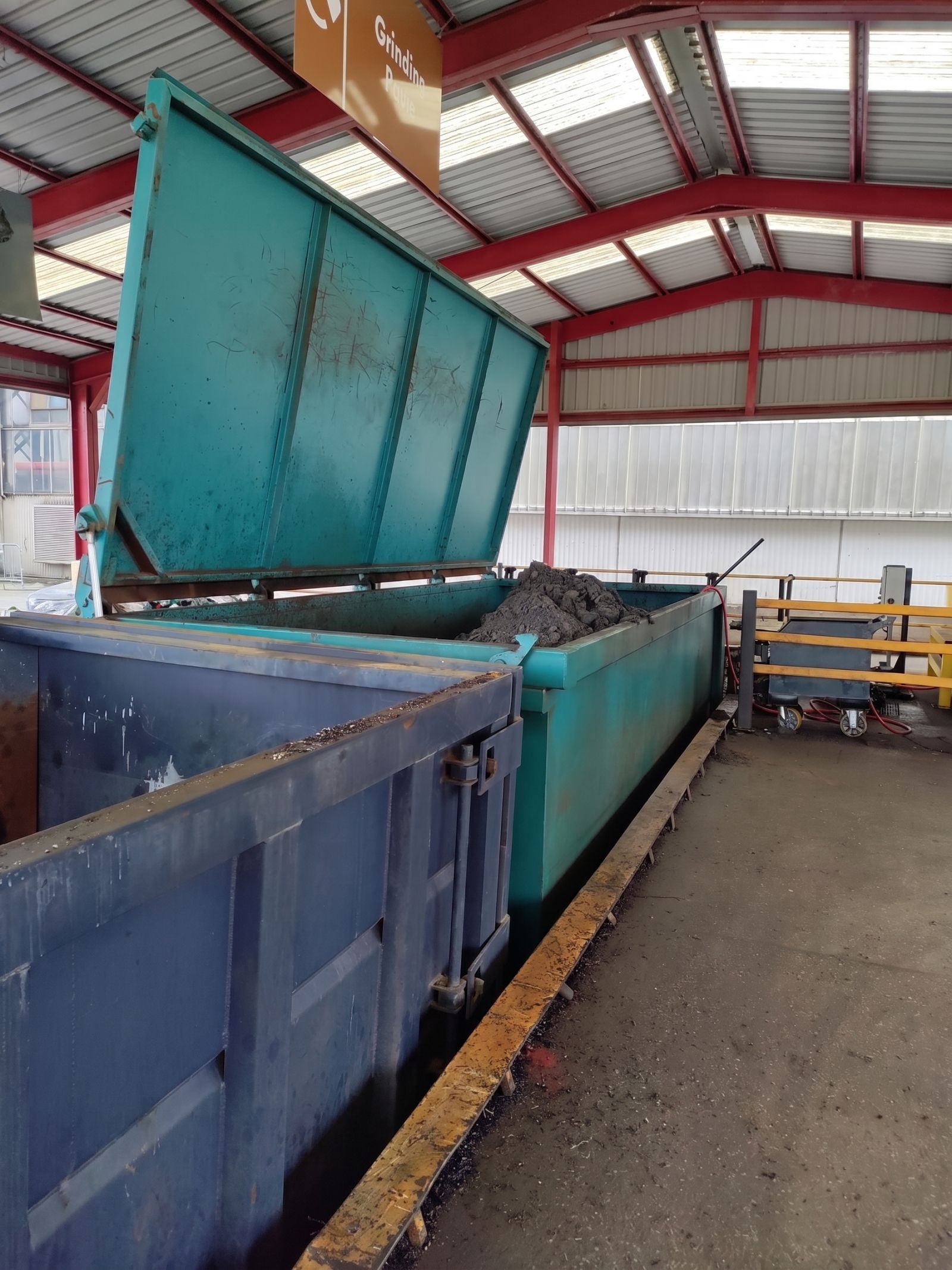 A lidded skip part-filled with interceptor sludge, its lid raised, standing in a covered bay at a waste transfer station.